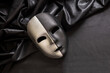Carnival Venetian two faced mask, half black half silver on dark satin textile background,