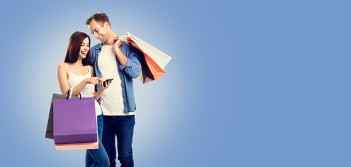 Wall Mural - Love, holiday sales, shop, rebates, discounts offers concept - happy smiling couple with shopping bags, and cellphone, standing close to each other. Blue color background.