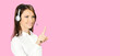 Call center service. Customer support female phone sales operator in white confident cloth, headset showing pointing clicking at copy space, imaginary or slogan text, over rose pink background.