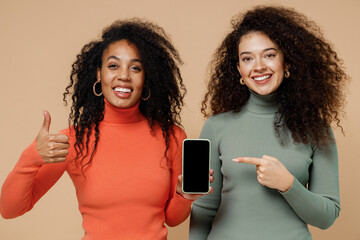 Canvas Print - Two young curly black women friends 20s in casual shirts clothes hold use mobile cell phone with blank screen workspace area show thumb up like isolated plain pastel beige background studio portrait.