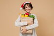 © ViDi Studio - Young cheerful fun woman 20s wear casual clothes christmas hat hold paper bag with vegetables isolated on plain pastel beige background studio portrait. Happy New Year 2022 concept Shopping concept.