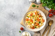 Pasta salad with ham, mozzarella, corn, tomatoes and olive oil in a ceramic plate on a light culinary background. Traditional Italian dish penne rigate with cheese and vegetables top view