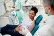 © Drazen - Happy African American woman talks to dentist during appointment at dentist's office.