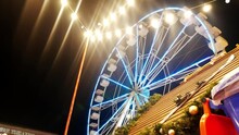 Flashing Ferris Wheel Ride Rotating Above Stall At City Christmas Fair At Night