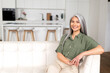 © Vadim Pastuh - Portrait of attractive middle-aged woman with long silver hair sitting in modern apartment, mid-aged multiracial asian female resting at home, looking at camera and smiling with wide toothy smile