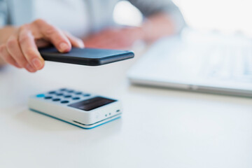 Businesswoman scanning QR code on mobile phone through card terminal at desk