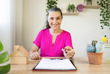 Smiling Female Real Estate Agent Offering Pen At Home Office