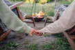 © Westend61 - Young couple holding hands while sitting on chair near fire pit