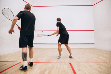 Full-length portrait of two young sportive men training, playing squash game in special sport studio. Back view