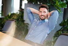 Smiling Mid Adult Businessman With Hands Behind Head Relaxing At Work Place