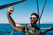 Young Man Taking Selfie Through Smart Phone In Yacht On Sunny Day