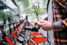 Young Man Using Smart Phone At Bicycle Parking Station