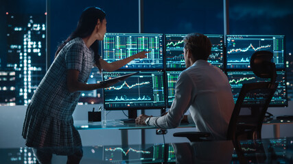Poster - Financial Analyst Talking to Investment Banker in the Evening at Work. Chatting About Real-Time Stock Chart Data on Multi-Monitor Workstation. Businesspeople Have a Meeting in Broker Agency Office.