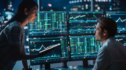 Poster - Financial Analyst Talking to Investment Banker in the Evening at Work. Chatting About Real-Time Stock Chart Data on Multi-Monitor Workstation. Businesspeople Have a Meeting in Broker Agency Office.