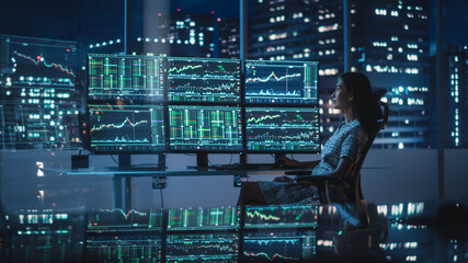 Financial Analyst Working on a Computer with Multi-Monitor Workstation with Real-Time Stocks, Commodities and Exchange Market Charts. Businesswoman at Work in Investment Broker Agency Office at Night.