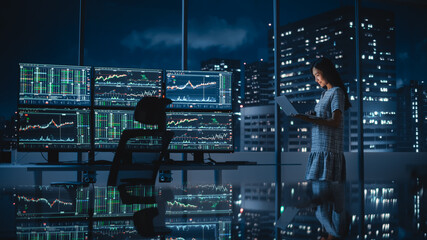 Poster - Financial Analyst Using Laptop Computer, Standing Next to Multi-Monitor Workstation with Real-Time Stocks, Commodities and Exchange Market Charts. Businesswoman Working in Investment Bank City Office.