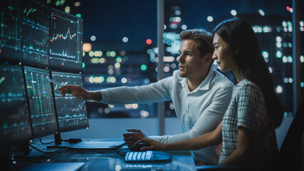 Poster - Financial Analyst Talking to Investment Banker in Late Evening at Work. Chatting About Real-Time Stock Chart Data on Desktop Computer. Businesspeople Have a Meeting in Broker Agency City Office.