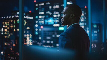 Poster - Successful Businessman Looking Out of the Window on Late Evening. Modern Hedge Fund Investor Enjoying Successful Life. Urban View with Down Town Street with Skyscrapers at Night with Neon Lights.