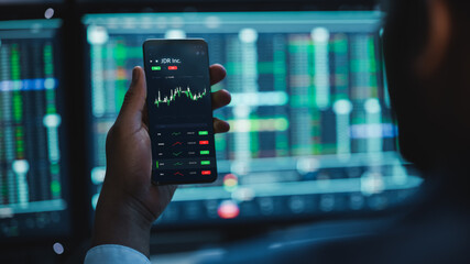Poster - Financial Analyst Using Smartphone with Real-Time Stocks, Commodities and Market Charts. Working on Multi-Monitor Workstation with Stock Charts. Businessman Works in Investment Bank in the Evening.