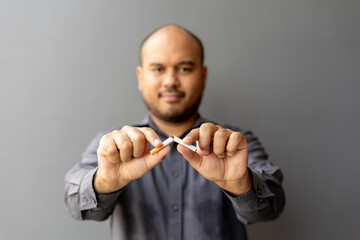 Portrait young man holding broken cigarette in hands. Happy male quitting refusing smoking cigarettes. Quit bad habit, Stop smoking cigarettes, health care concept. No smoking campaign.