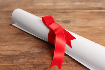 Wall Mural - Rolled student's diploma with red ribbon on wooden table, closeup