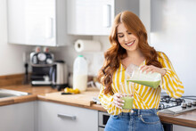 Smiling Redhead Woman Pouring Healthy Milkshake While Standing In Kitchen At Home