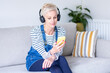 © Westend61 - Mature woman listening music through headphones while sitting on sofa at home