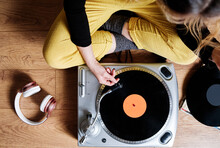 Woman Adjusting Tonearm Of Turntable While Sitting On Floor At Home