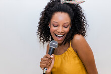 Cheerful Young Woman Singing While Holding Microphone Against White Background