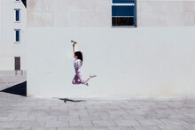 Young Woman With Megaphone Jumping By Building During Sunny Day