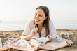 © Westend61 - Thoughtful happy woman holding pen while resting at beach