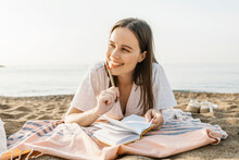 Thoughtful Happy Woman Holding Pen While Resting At Beach