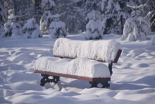 Wooden Bench In The Park Covered With A Thick Layer Of Snow On A Winter Sunny Day. Snow Cover. Natural Winterly Background