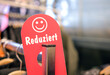 Nahaufnahme eines roten Schildes mit der Aufschrift „Reduziert“ und Smiley an einem Kleiderständer in einem Modegeschäft – selektiver Fokus, Copy Space