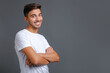 © Serhii - Handsome young unshaved man in white t-shirt with crossed arms looking at camera against gray wall and smiling. Satisfied caucasian guy looking at camera with a big laugh, copy space