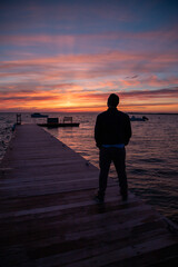 Wall Mural - Silhouette of man standing on dock watching sunset over the ocean.