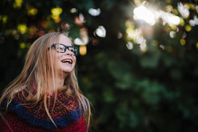Little Girl With Long Hair And Glasses Laughs In Front Of Fall Foliage