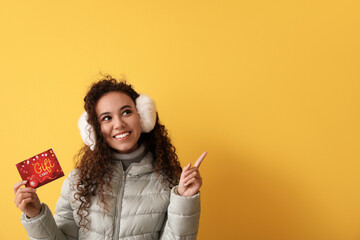 Wall Mural - Young African-American woman with gift card pointing at something on color background