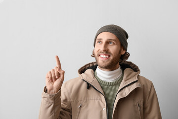 Sticker - Handsome young man in winter clothes pointing at something on light background