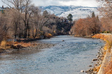 Wall Mural - Truckee River near Wingfield Park in downtown Reno, Nevada in late autumn. Barren trees, Snowcapped mountains and cloudy skies are in the background. 