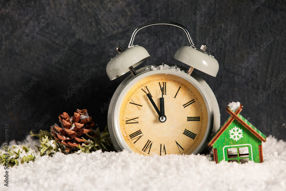 Alarm clock, Christmas decoration and pine cone on snow against dark background