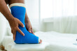 © Ekkasit A Siam - The man's hand was holding the right leg that had suffered a fractured bone and put a blue cast wrapped around the leg from foot to shin in a white bedroom.