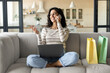 © Prostock-studio - Lovely young brunette woman with gift bags shopping online on laptop, confirming web order on smartphone from home