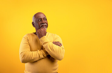 Thoughtful senior black man looking aside at empty space, touching his chin, deep in thought on orange background