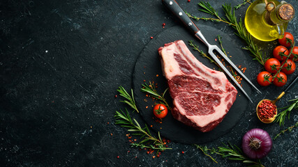 Wall Mural - Raw beef ribeye steak on the bone with thyme, rosemary and spices. Top view. Flat lay top view on black stone cutting table.