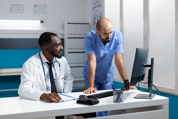 Team of medical therapists monitoring sickness symptoms expertise on computer discussing healthcare treatment. African american physician doctor working at medicine prescription in hospital office