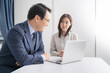 © rrice - オフィスでノートパソコンを見ながら打ち合わせをする男女のビジネスマン