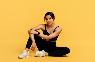 Wall Mural - Wellness and training. Happy sporty african american woman sitting on the floor at yellow studio background