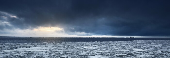 Wall Mural - Empty promenade and snow-covered breakwaters close-up, frozen Baltic sea in the background. Dark storm clouds. Winter, seasons, climate change, global warming concepts. Long exposure