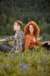 © alfa27 - Smiling couple hiking in summer mountains in countryside. Happy woman and man sit on grass. Female and male tourists in casual wear exploring nature. Side view portrait. Nature, people concept
